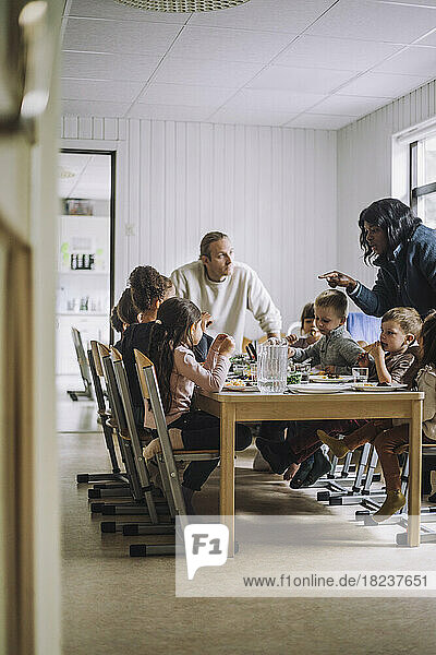 Lehrerinnen und Lehrer im Gespräch mit Kindern beim Frühstück am Esstisch
