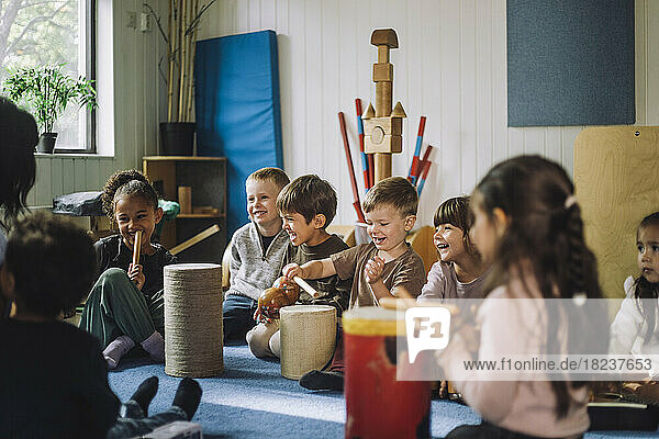 Happy multiracial male and female students enjoying while playing drum kit in child care center