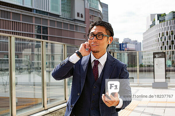 A young businessman in the city  on the move  a man in a suit  holding a mobile phone and using a handset at his ear.
