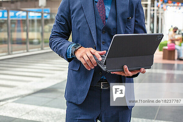 A young businessman in a blue suit on the move in a city downtown area  standing and using his digital tablet.