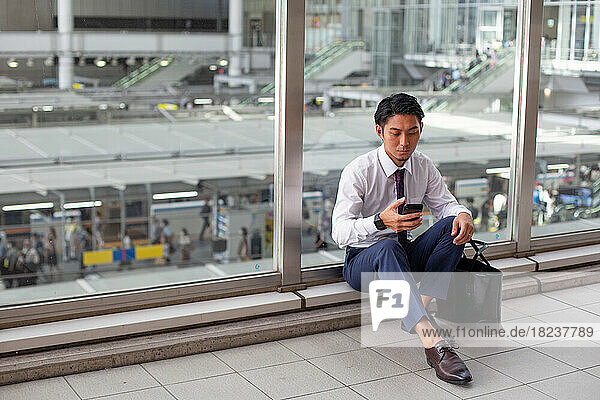 A young businessman in the city  on the move  sitting on a walkway  looking at his phone.