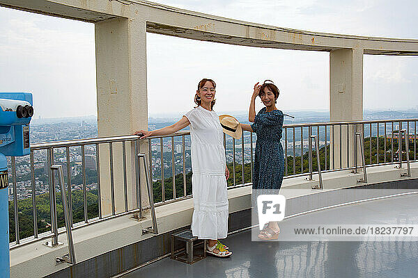 Two mature Japanese women at a viewing platform outdoors in summer  leaning on the rail.