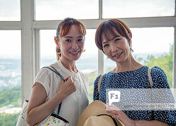 Two mature Japanese women  friends  side by side  on a day out  looking at the camera.