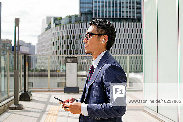 A young businessman in the city  on the move  a man in a blue suit holding a mobile phone  standing on an elevated walkway.