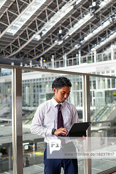 A young businessman in the city  on the move  standing on a walkway  using his laptop.