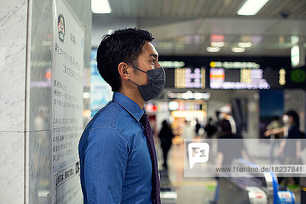 A young businessman in the city  on the move  standing at a metro station  wearing a face mask.