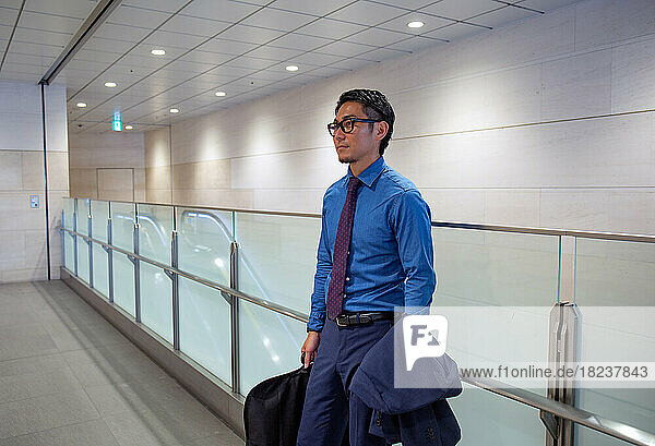 A young businessman in the city  on the move  a man standing on a walkway carrying a suit carrier and a hacket.