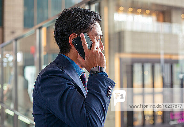 A young businessman in a blue suit on the move in a city downtown area  speaking on his mobile phone.