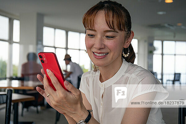 A mature Japanese woman looking at her phone screen and smiling  sending a text  messaging.