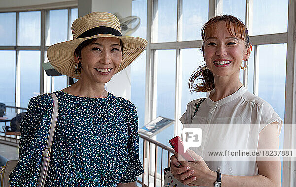 Two mature Japanese women  friends  side by side  on a day out  looking at the camera.