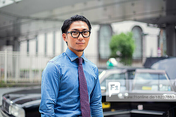 A young businessman in the city  on the move  a man with eyeglasses  shirt and tie  a taxi behind him.