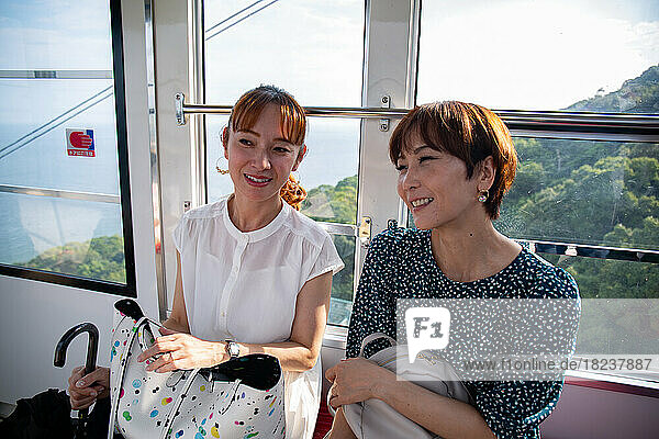 Two mature women seated side by side in a cable car  friends on a day out.