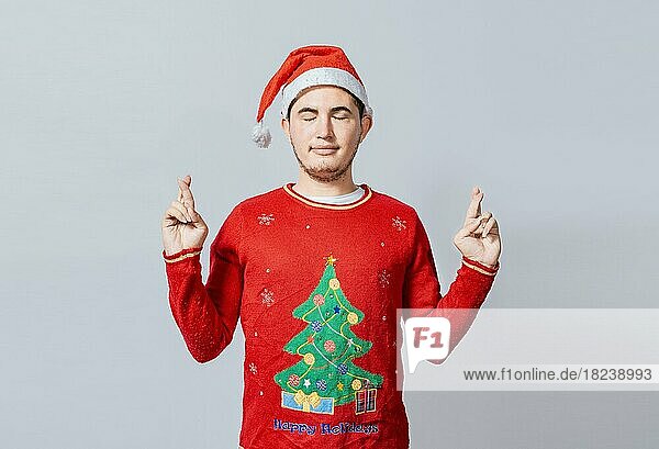 Hoffnungsvoller Mann in Weihnachtskleidung wünscht sich etwas  Schöner Mann mit Weihnachtsmütze wünscht sich etwas auf weißem Hintergrund  Mann mit Weihnachtsmütze wünscht sich etwas auf isoliertem Hintergrund