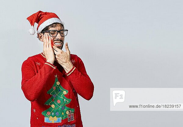 Mann im Weihnachtspulli mit Zahnschmerzen  Junger Mann in Weihnachtsmütze mit Zahnschmerzen isoliert  Mann mit Weihnachtsmütze in Schmerzen berührt seinen Zahn. Weihnachten Zahnschmerzen Konzept