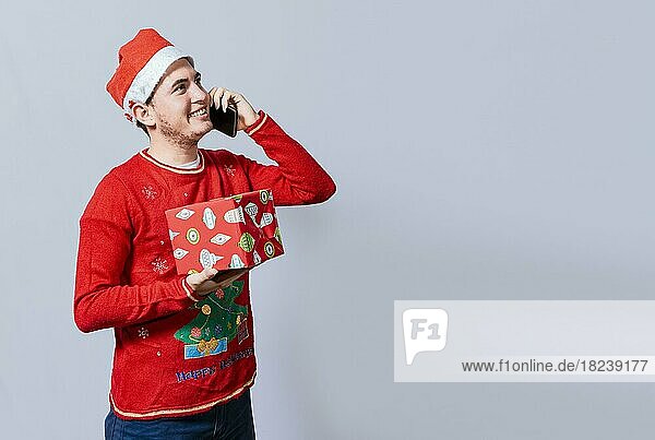Weihnachten Mann hält Geschenk und ruft Familie am Telefon. Happy man holding gift and calling family at christmas  Smiling guy in christmas hat holding christmas gift box and talking on the phone