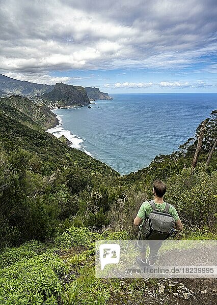 Wanderer blickt in die Ferne  Ausblick auf steile felsige Küste und Meer  hinten Ort Porto da Cruz und Adlerfelsen Penha de Aguia  Küstenlandschaft  Wanderweg Vereda do Larano  Madeira  Portugal  Europa