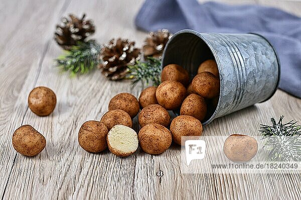 Traditionelle deutsche Weihnachtsbonbons  genannt Marzipankartoffeln. Runde  kugelförmige  mit Zimt und Kakaopulver bestreute Mandelpastetchen  die aus einem Eisenbecher auf Holzuntergrund quellen