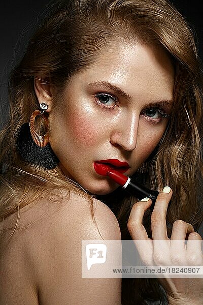 Schönes Mädchen mit roten Lippen und klassischen Make-up und Locken mit Lippenstift in der Hand. Schönes Gesicht. Foto im Studio aufgenommen
