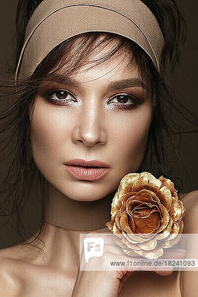 Schöne Frau mit einem hellen Make-up und perfekte Haut mit goldenen Blumen in der Hand. Schönes Gesicht. Bild im Studio auf einem schwarzen Hintergrund aufgenommen