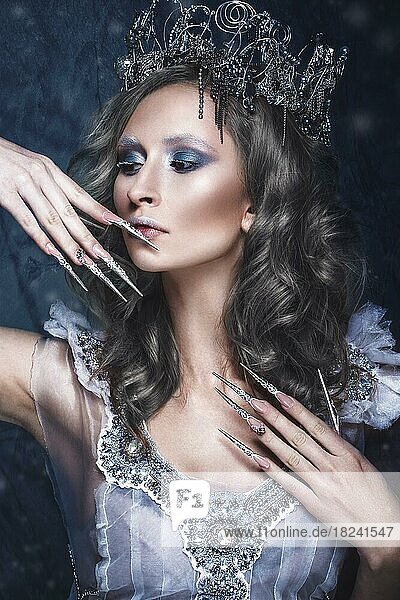 Schönes Mädchen im Bild der Schneekönigin mit kreativem Make-up in einem transparenten Kleid mit einer Krone und einer langen Nagelkunst. Die Schönheit des Gesichts. Fotos im Studio geschossen