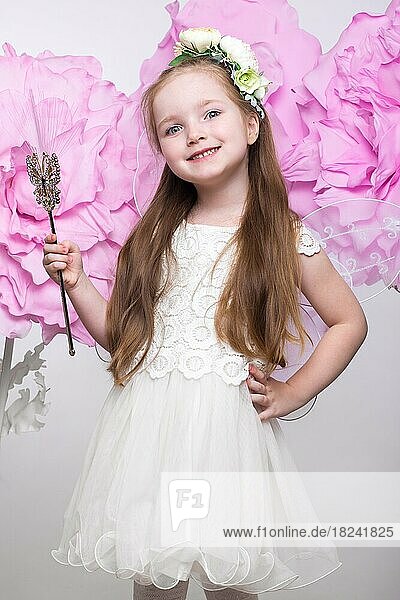 Little fairy girl in white dress on a background of flowers. Photo taken in studio