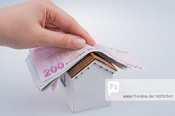 Hand hält türkische Lira-Banknoten auf dem Dach eines Modellhauses auf weißem Hintergrund
