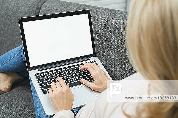 Close up blonde woman sitting sofa using laptop with blank white screen