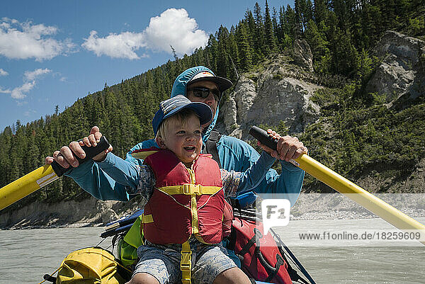 A father and son row a raft down a large river in the mountains