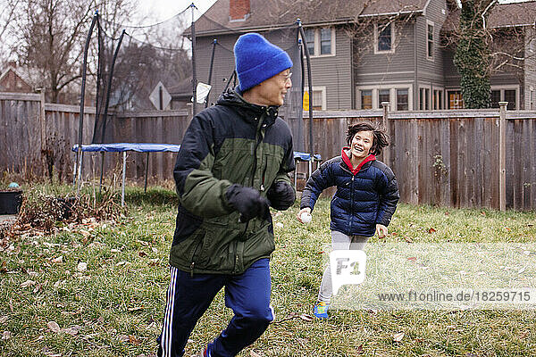 A happy boy chases father through yard in winter
