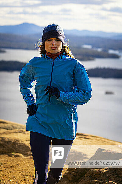 A woman in a blue jacket runs with a lake in the background.
