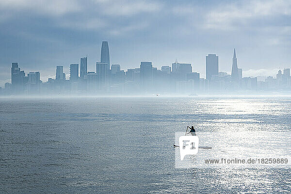 woman paddleboarding in bay with city skyline