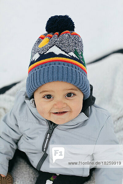 happy toddler boy with brown eyes smiling at camera in snowsuit