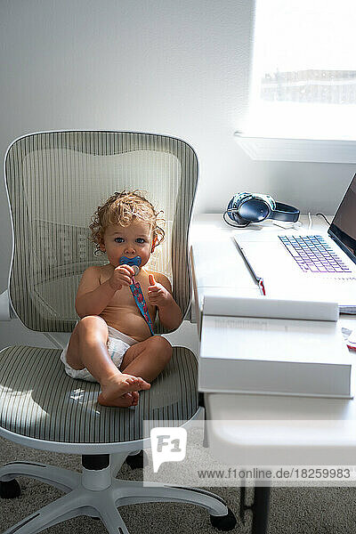 Cute baby boy with pacifier and laptop on the table