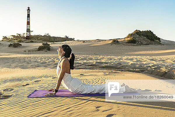 A woman lying on a mat in a stunning dune near a lighthouse