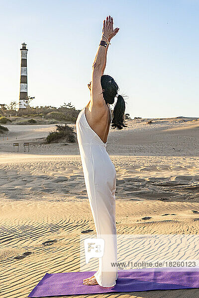 Side view of a female standing with arms up doing sun salutations