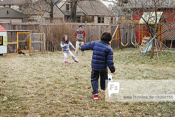 Two children play soccer with father in yard with chickens