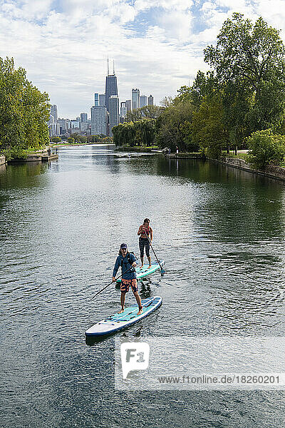 Man and woman paddleboarding in river with city in background
