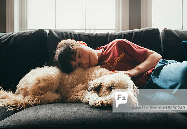 Cute happy boy and fluffy dog laying together on the sofa.