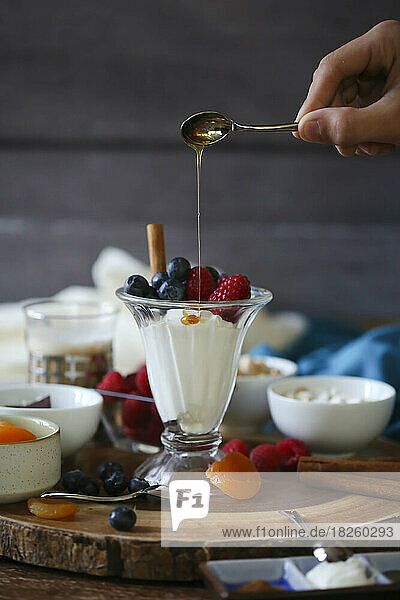 Fruit and yogurt parfait with dripping honey on wood background