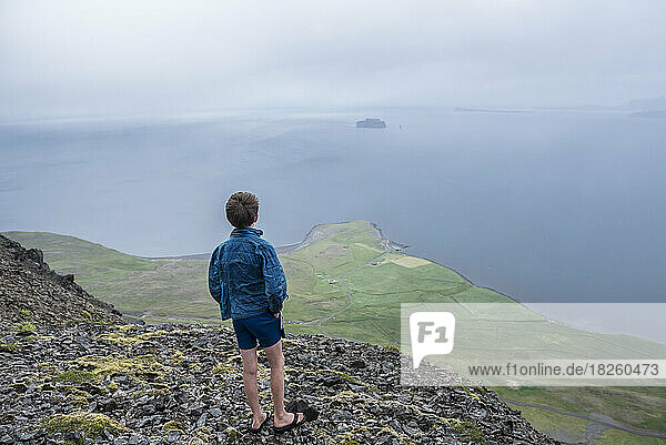 A boy looks out to the Greenland Sea from a mountain top in Iclenad
