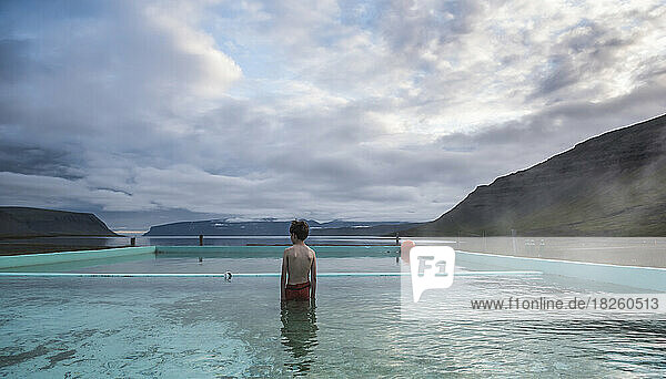 a boy stands in a hot spring in the Westfjords of Iceland