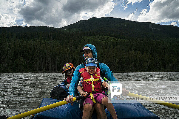 A father and his son and daughter in a raft on a wide river