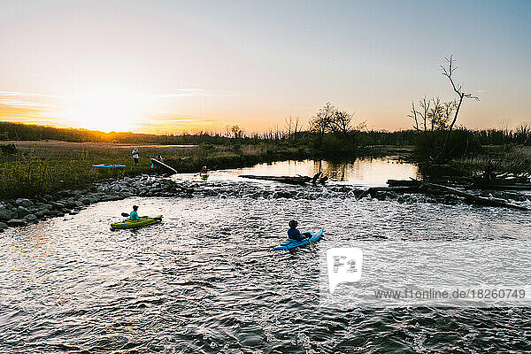 People kayak in river as sun sets in the summer over wetlands