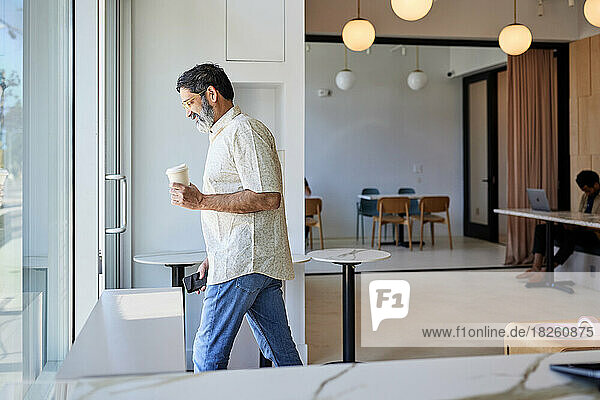 Smiling mature man with disposable coffee cup leaving coffee shop