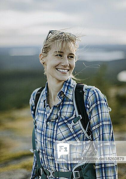 Blonde young woman in flannel shirt smiles while hiking in Maine
