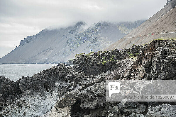 A man walks on rocks above the ocean on the south coast of Iceland.