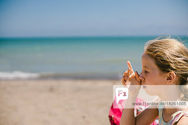 Girl in bathing suit rubs sun screen into her face and nose at beach