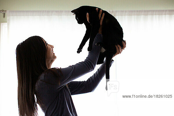 Teen Girl Holds Black Cat Up And Smiles