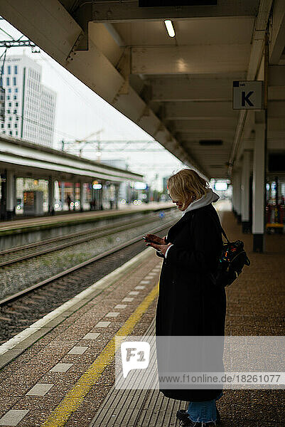 Woman on the rialway station platform looking with the phone in hands