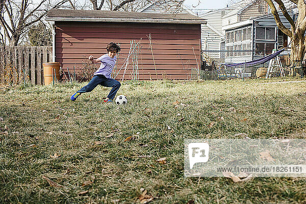 An athletic boy kicks soccer ball alone in backyard